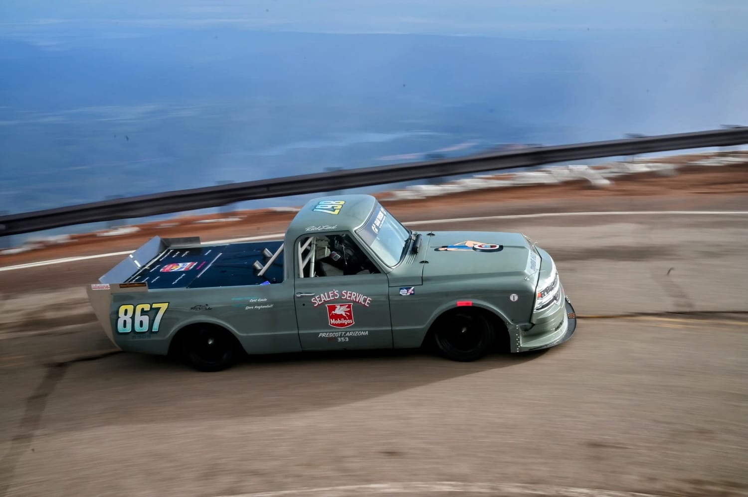 The No. 867 truck at speed on the Pikes Peak highway, guardrail and sky behind it